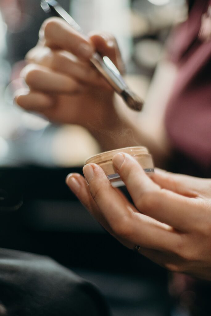 A detailed close-up of hands applying makeup using a brush in an artistic setting.