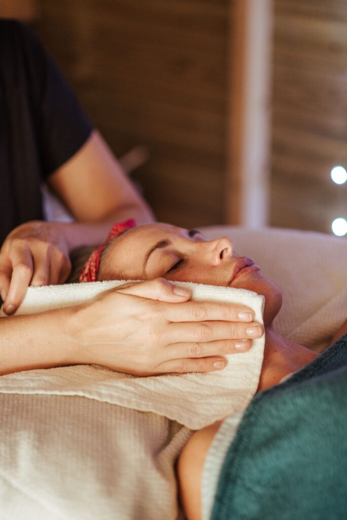 Adult lady lying in spa center while getting face massage from massager in spa salon